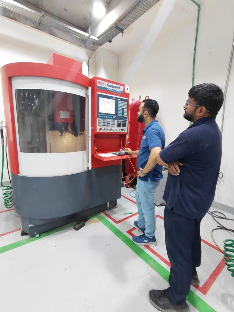 Operators at an Emco Concept Mill 250 CNC milling machine in a technical workshop