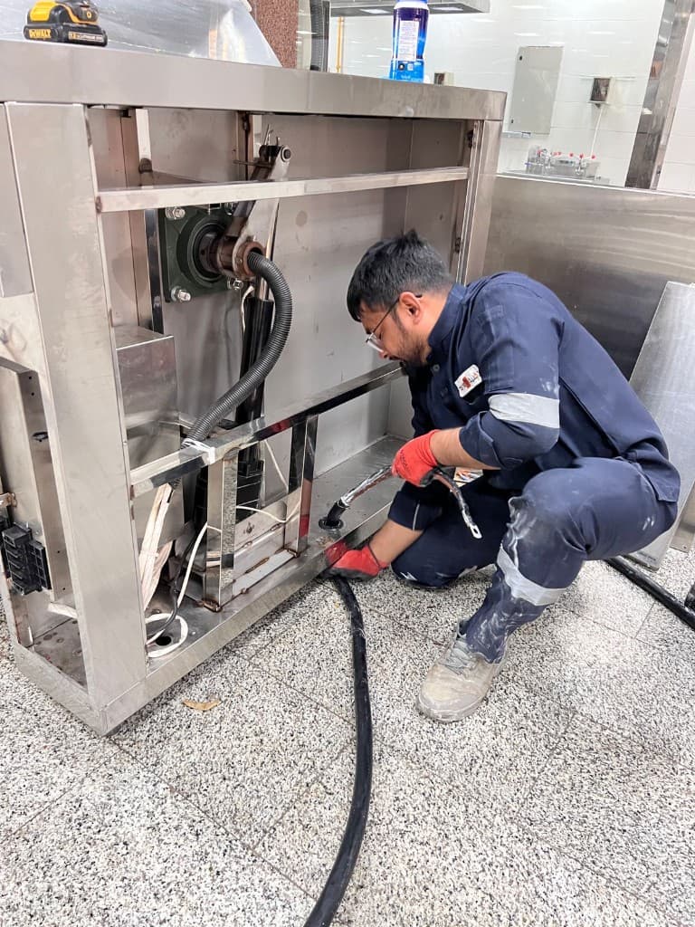 Technician servicing stainless steel commercial kitchen equipment on site