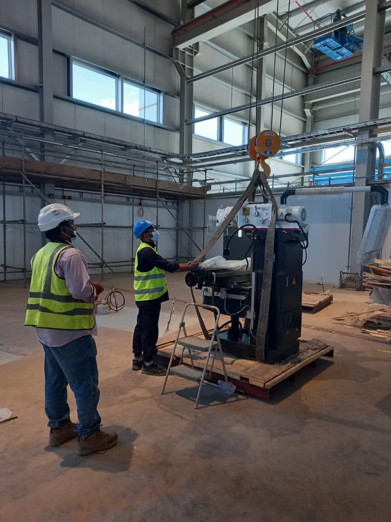 Technicians in PPE guiding a heavy machine during hoist lifting and installation